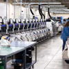 Industrial warehouse facility with rows of automated sorting machines and a worker in blue uniform monitoring operations