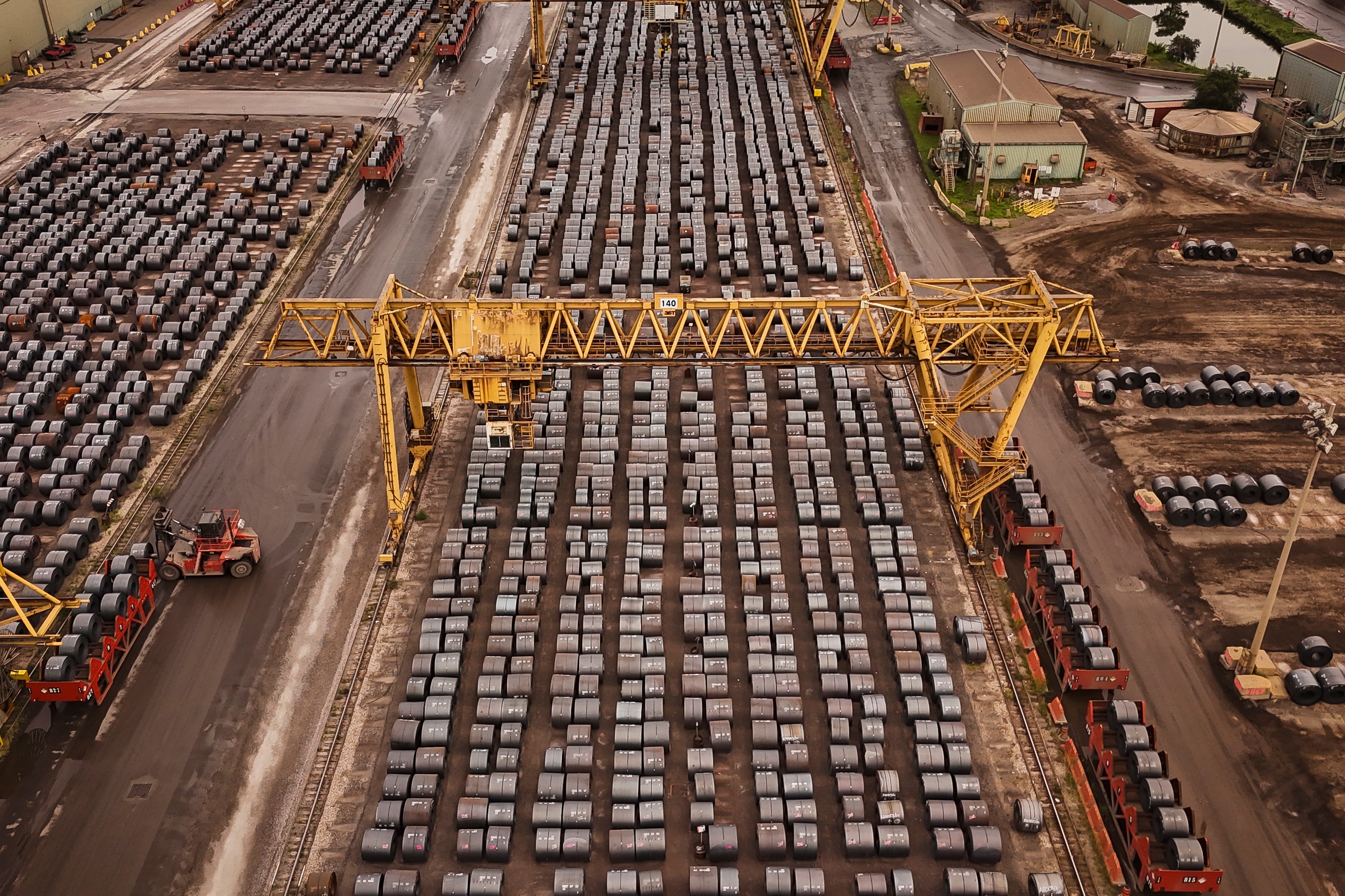 Aerial view of busy shipping port with hundreds of stacked containers, yellow gantry cranes, and cargo handling equipment