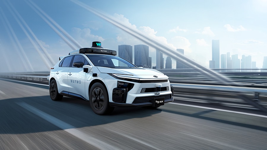 White autonomous taxi vehicle with blue accents driving on elevated highway with city skyline in background