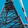 Tall telecommunications tower with red and white striped antenna against clear blue sky