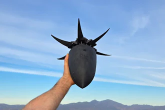 Person holding black spiked helmet against blue sky with mountains in background
