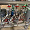 Industrial stainless steel multi-valve manifold system with red handles mounted on frame in workshop